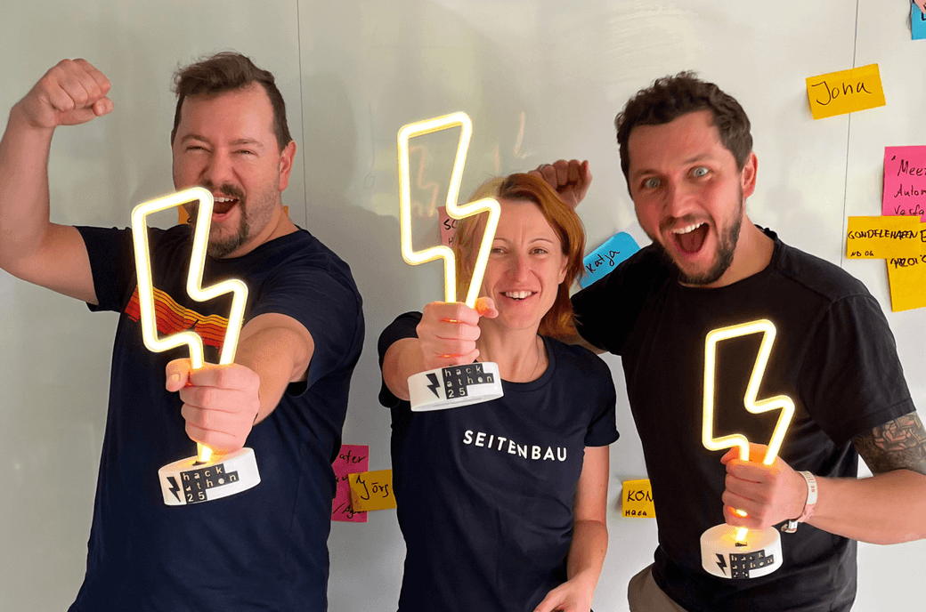 Drei Hackathon-Organisator*innen von SEITENBAU mit den leuchtenden Blitzen in der Hand, die später als Pokale an die Sieger*innen überreicht werden.